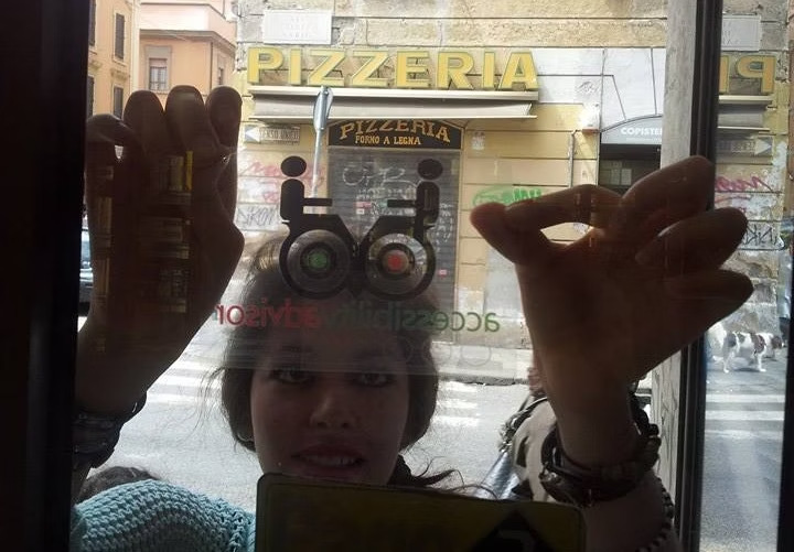 Una persona mostra l’adesivo Accessibility Advisor sulla vetrina di un esercizio commerciale.